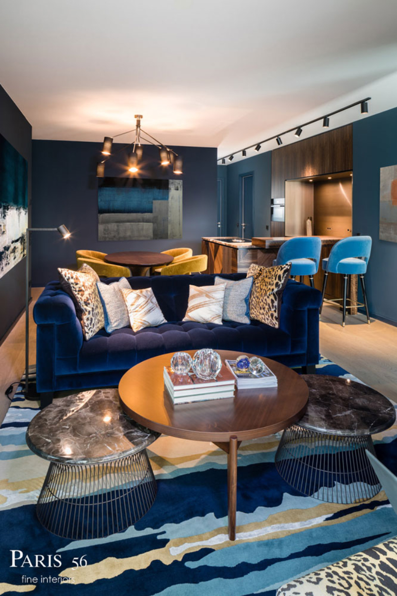 Paris 56 Fine Interiors with Fine Rugs; Apartment PANDION THE HAUS / Berlin Apartment; living room with a dark blue sofa, 2 baby blue counter stools and 4 yellow dinning chairs, along with a ruh with all this colors.