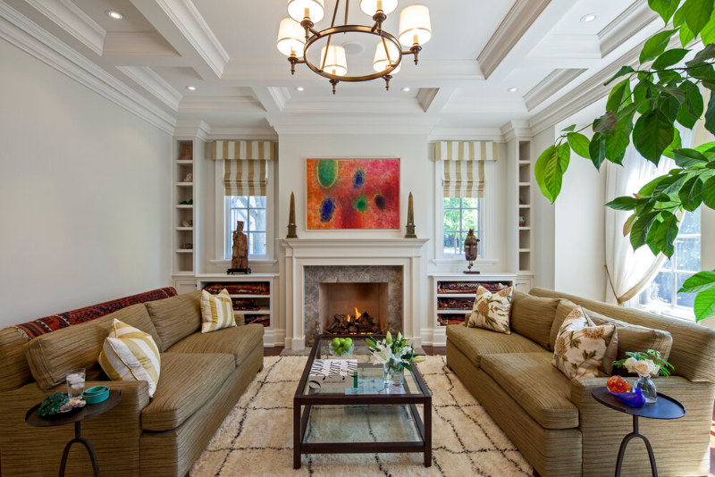 The living room designed by Douglas Design Studio has a serene color scheme. Both of the sofas are light brown and in the middle of the sofas is a coffee table. The center of this living room is the fireplace.