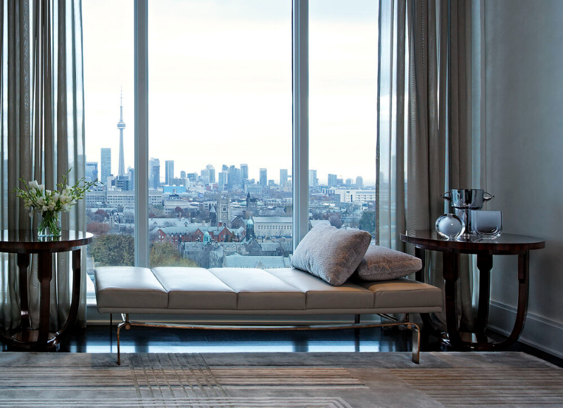 This corner in front of a window design by Douglas Design Studio is subdividing the space into different living areas. This area is to enjoy the view alone by the chaise longue and two pillows in grey. Next to the chaise longue are two round coffee tables.