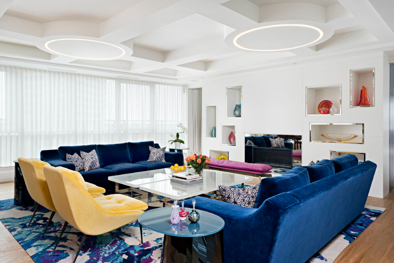This living room design by Douglas design studio is full of colors where the blue sofas contrast with the yellow armchairs and combine perfectly with the rug full of color too.
