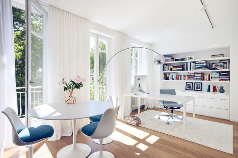Gabriela Raible Innenarchitektur home office with a round table, 3 chairs around it with blue cushions, a desk and a baby blue desk chair with a white rih underneath