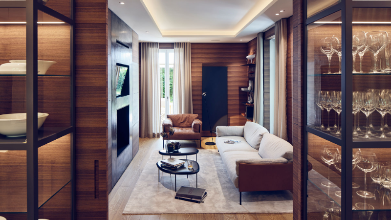 Gabriela Raible Innenarchitektur living and dining with a white sofa, an armchair, 2 metal center tables, walls covered in wood, a fireplace, and a rug.