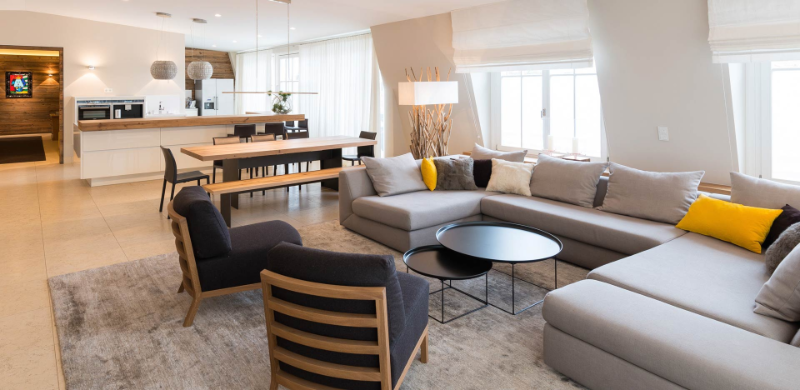 Gabriela Raible Innenarchitektur open living Munich with a grey rug, a white/grey sofa, 2 armchairs in wood, and 2 round metal center tables
