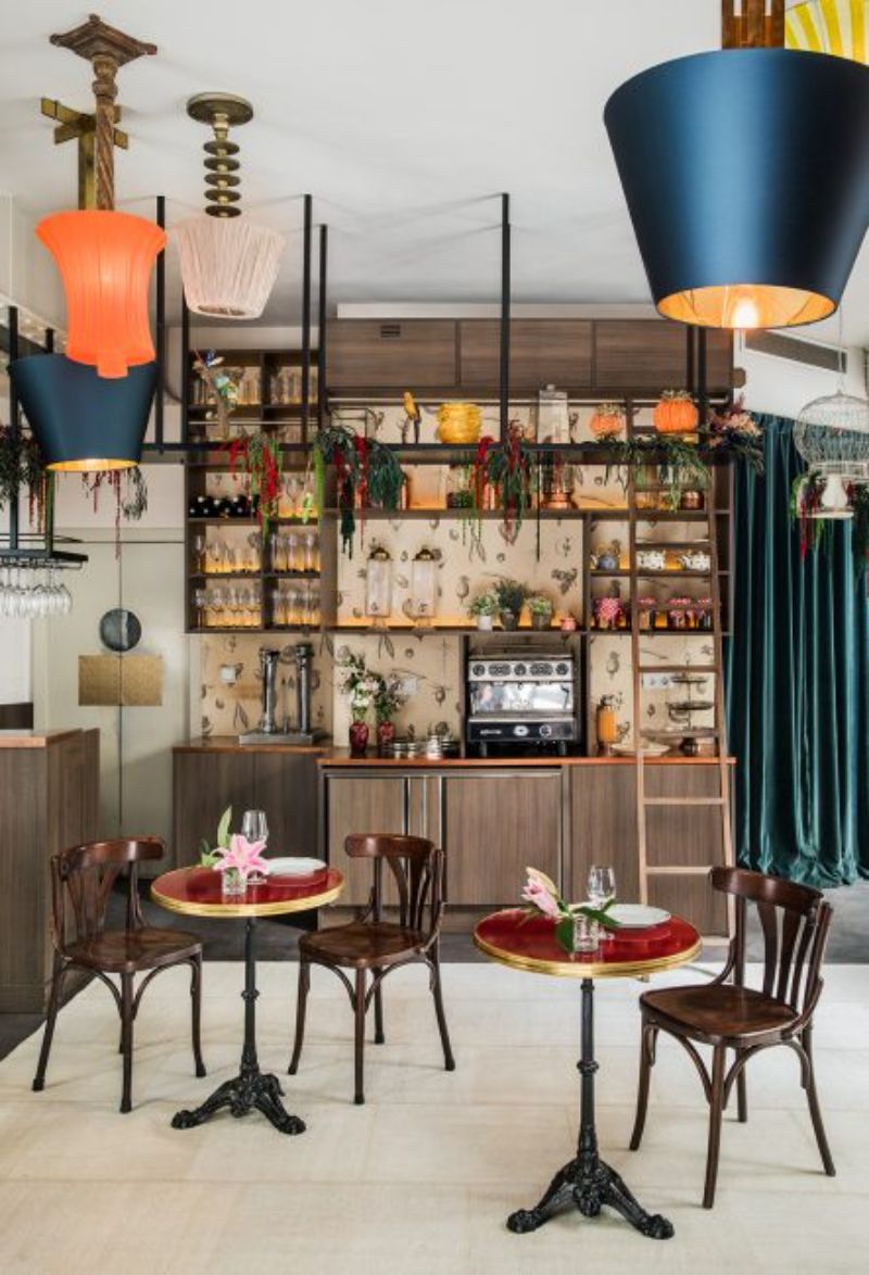 Restaurant by Ines benavides with red sofa and wooden chairs, colomful suspension lamps, white rug