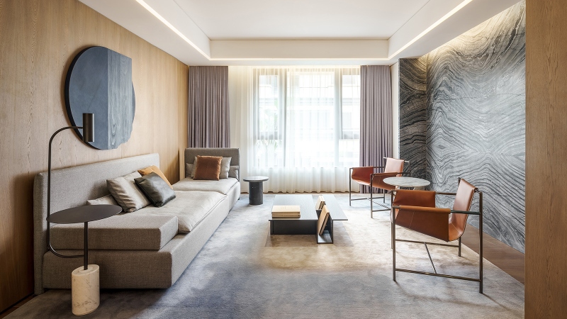 Rug designs from Mason Studio. This living room has blue wall, two chairs in orange, grey sofa and a rug in grey that covers all the room.