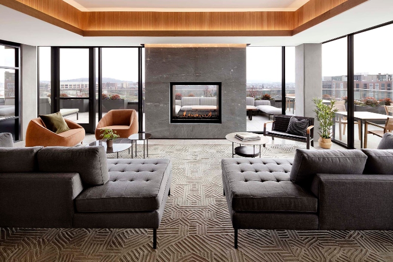 Rug designs from Mason Studio. This living room has two grey sofas, two orange armchairs, a black coffe table and a grey geometrical rug that covers all the room.