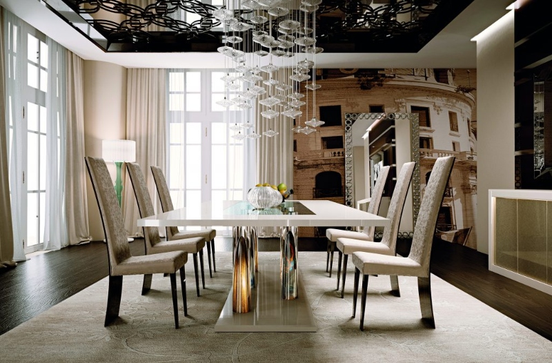 Rug Décor with Import Temptations. This dining room has a suspension chandelier, a white dining table, white dining armchairs, and a neutral rug.