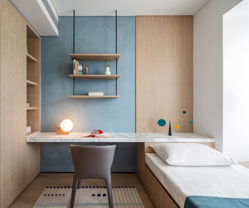 Rug designs from Mason Studio. This kids bedroom has light blue walls, a white marble table, a grey office chair and a rug in white with black and blue lines and dotts.