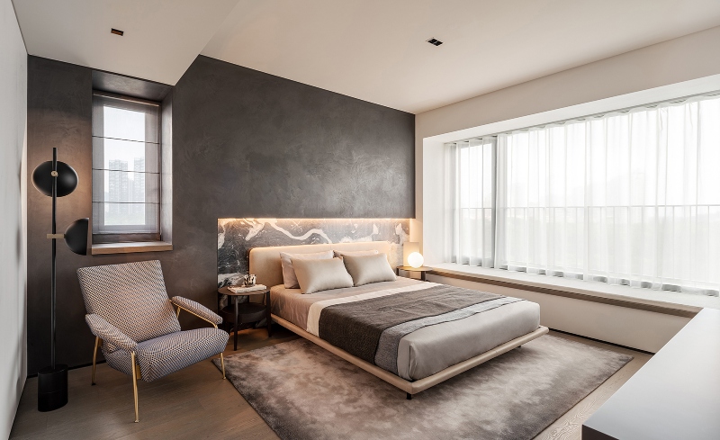 Rug designs from Mason Studio. This bedroom has one wall grey and the olthers are white, a a black floor lamp, a blue and white armchair, a white bed frame and, a grey and white rug.