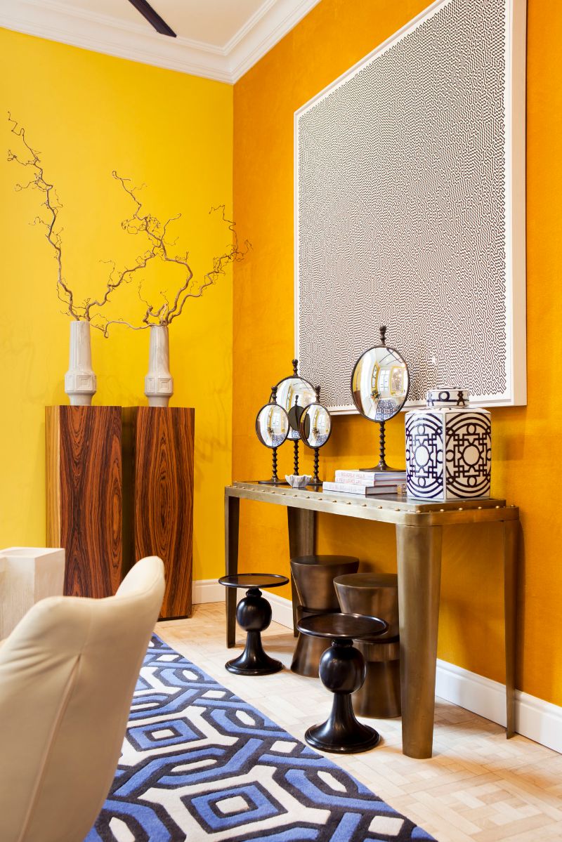 yellow walls, black and white decorative elements, golden console, blue and white rug
