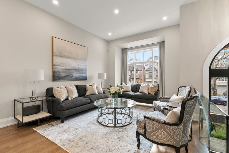 Rug Design Inspiration by Camden Lane Interiors. This neutral living room has two dark grey sofas, two armchairs in grey with white flowers, a center table in glass with a gold structure and a white rug.