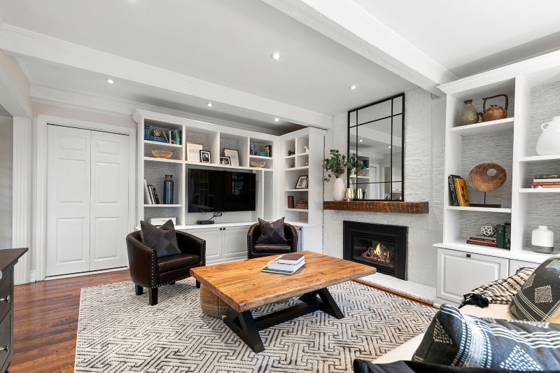 Rug Design Inspiration by Camden Lane Interiors. This white living room with a white fireplace and white shelves has two leader brown armchairs, a wood coffee table and a rug in white with black lines.
