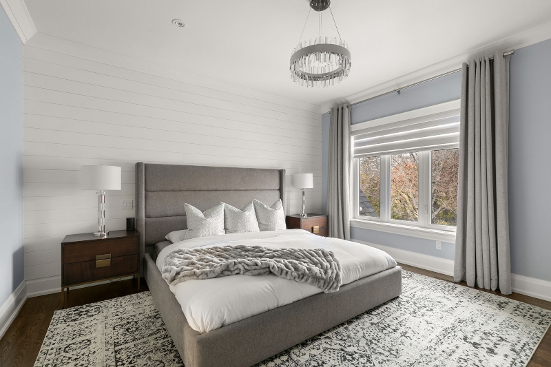 Rug Design Inspiration by Camden Lane Interiors. This white bedroom with two blue walls has a bedframe in grey, two side tables in wood, and a white and grey rug.