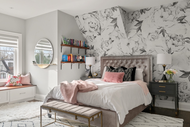 Rug Design Inspiration by Camden Lane Interiors. This white bedroom has wallpaper with flowers in grey and white, a pink bed frame and bench, a green side table, and a rug in white with black lines.